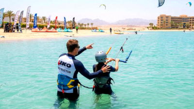 Instructor certificado IKO ayudando a un estudiante en aguas hasta la cintura en una escuela de kitesurf Hurghada
