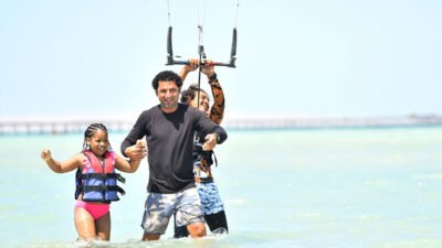 Beginners practicing kitesurf safety quick-release activation on a sandy beach.